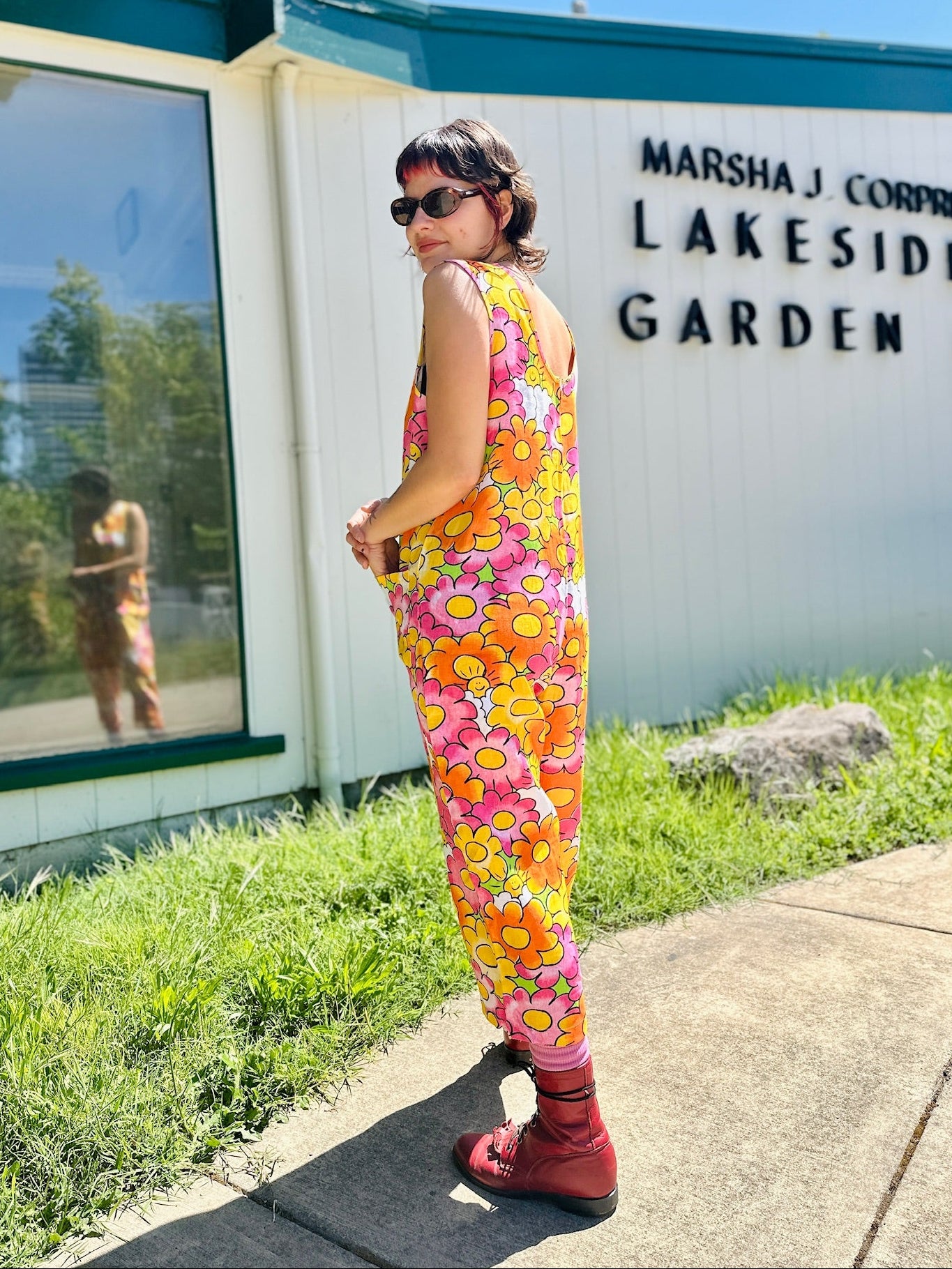 Person wearing a colorful floral jumpsuit standing in front of a building with 'Lakeside Garden' sign.