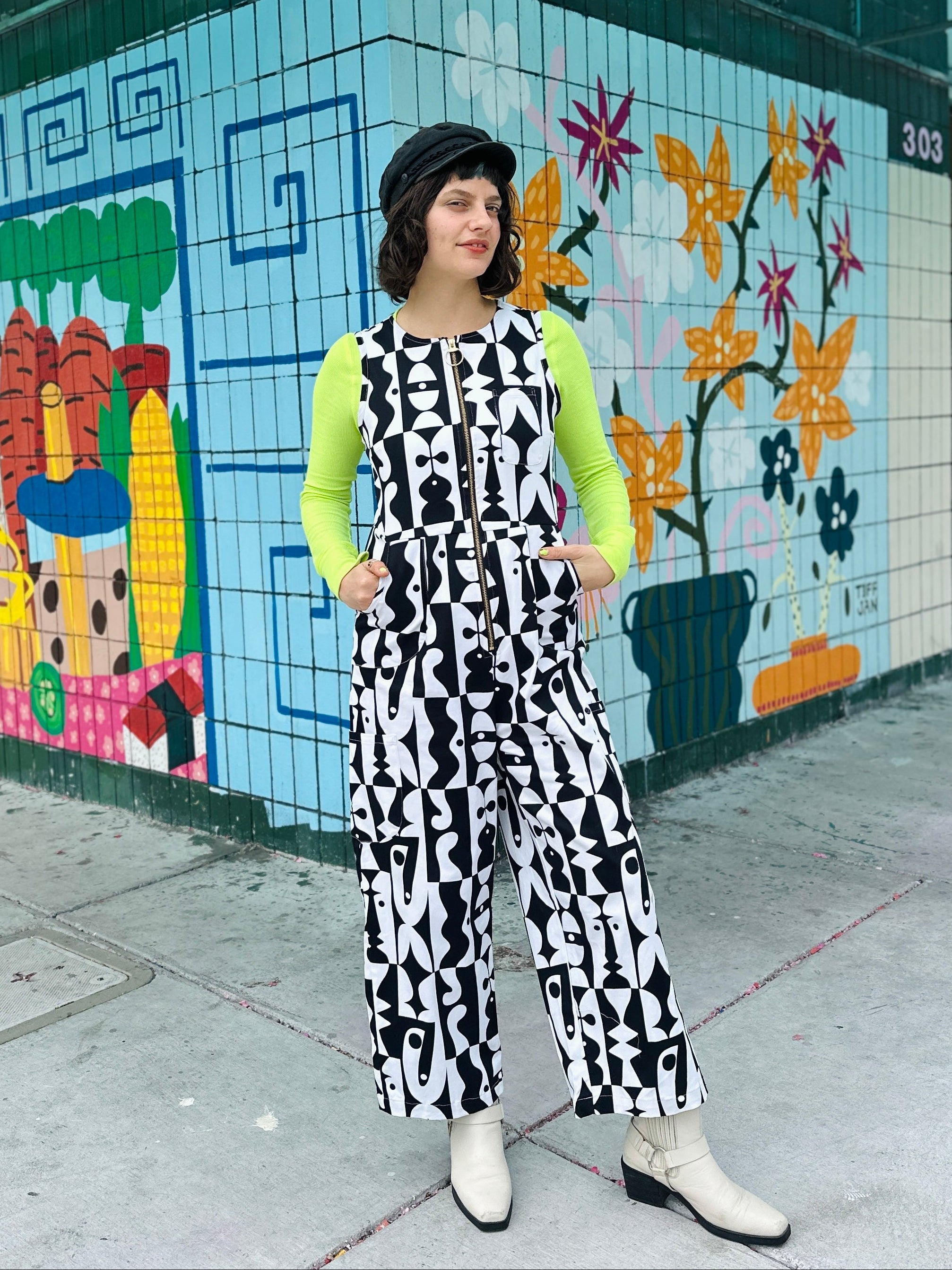 Person wearing a black and white patterned jumpsuit in front of a colorful mural.