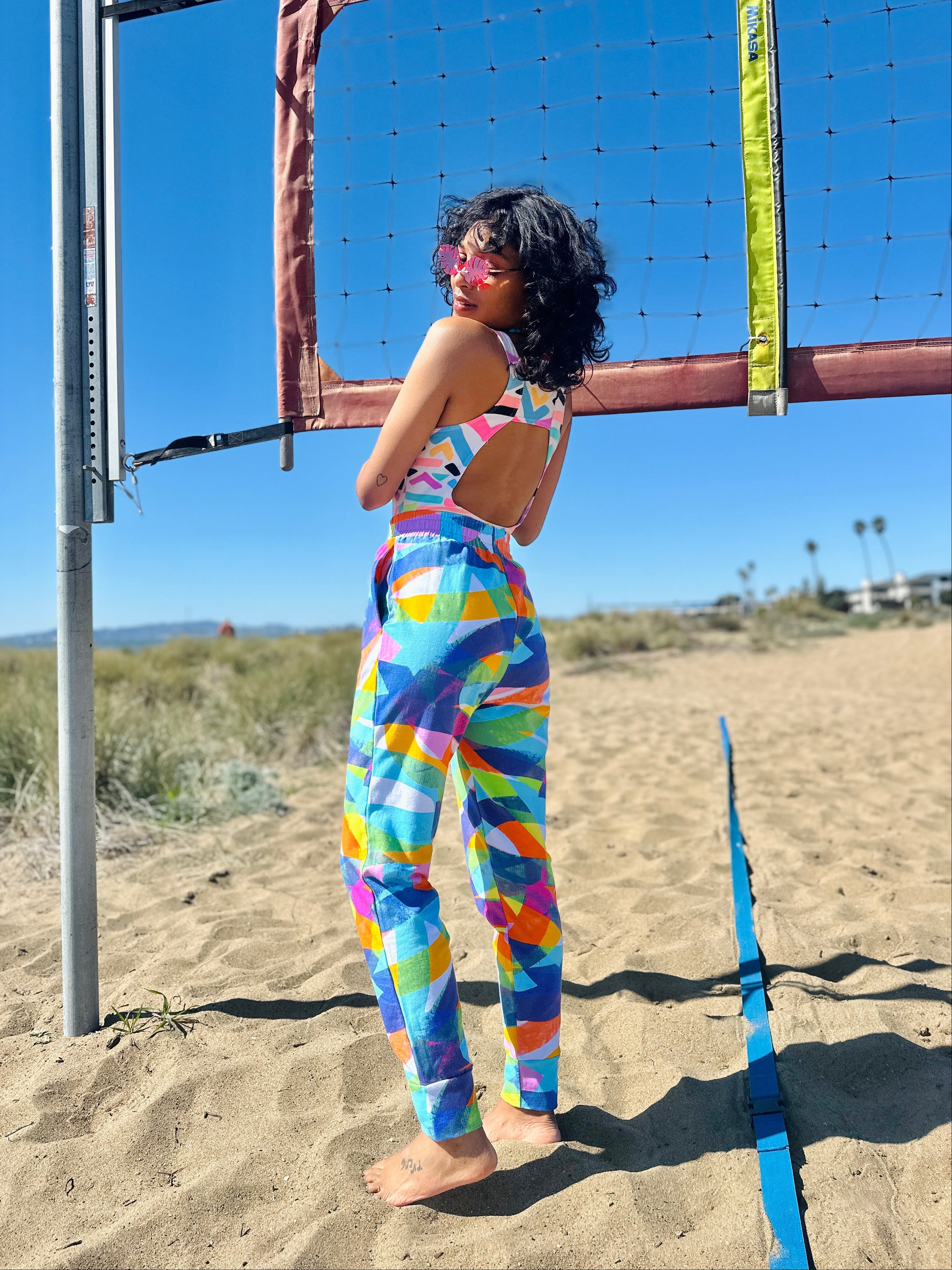 Person in colorful outfit standing on a beach next to a volleyball net