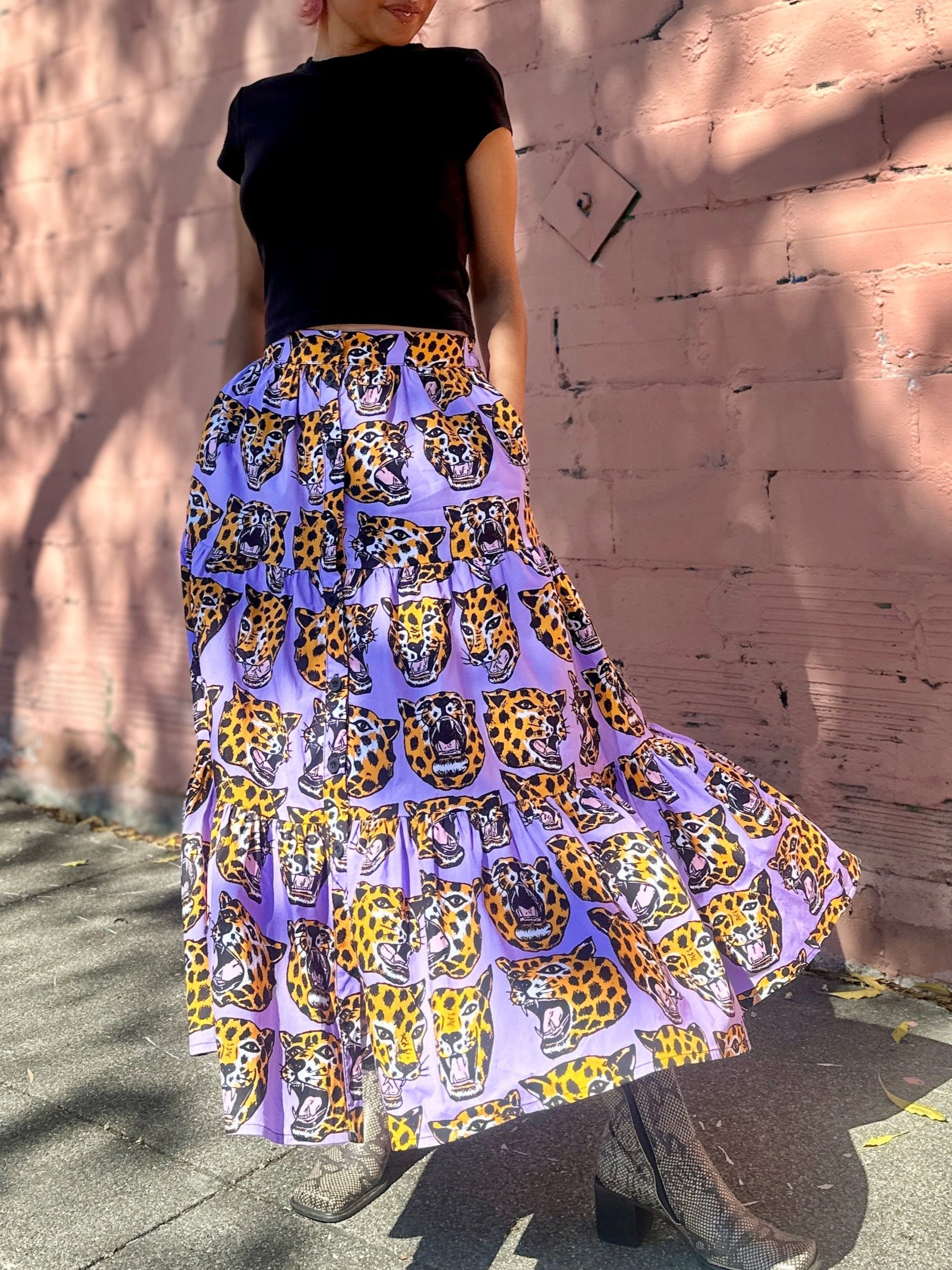 Person wearing a black top and colorful patterned skirt standing against a textured wall.