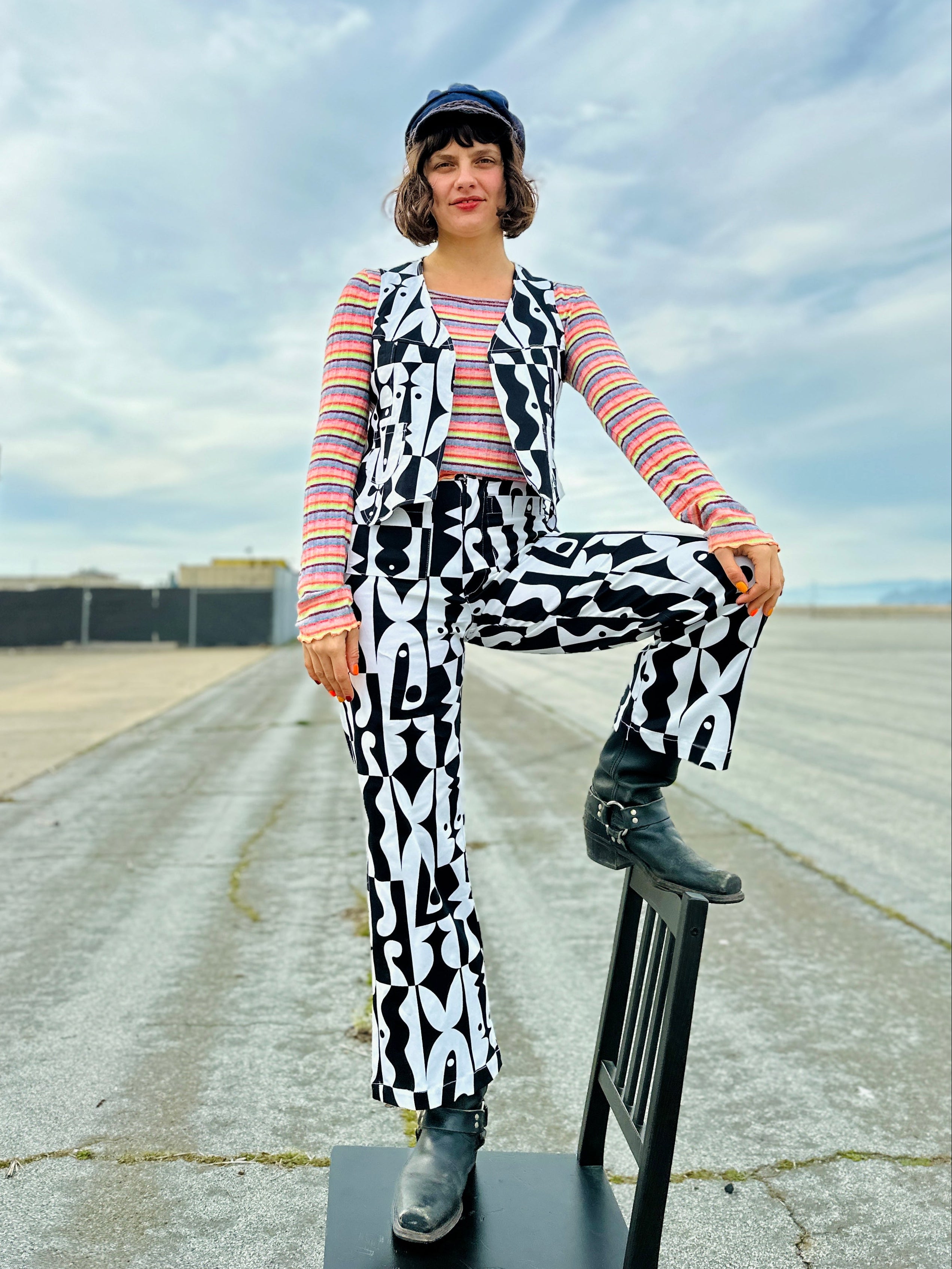 Person wearing a colorful outfit with black and white patterned pants, sitting on a chair outdoors.