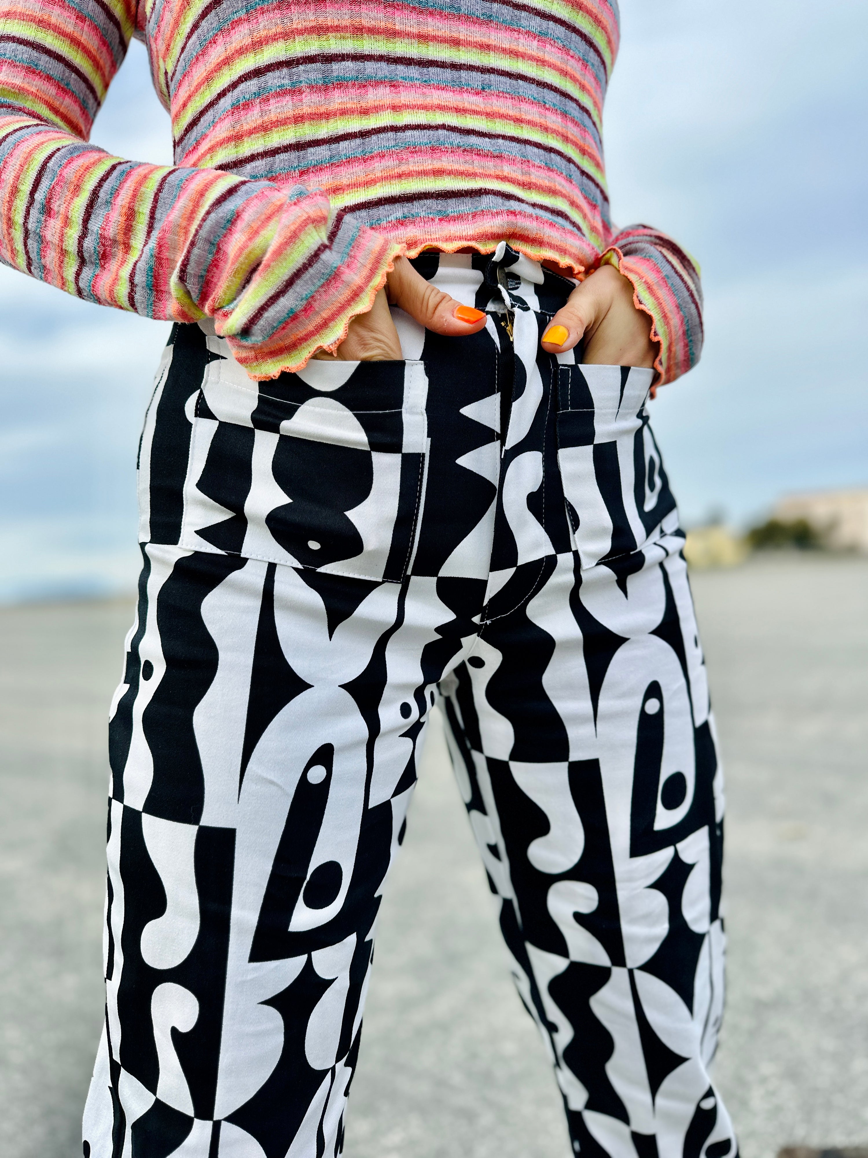 Person wearing a colorful striped sweater and black and white patterned pants with a blurred background.