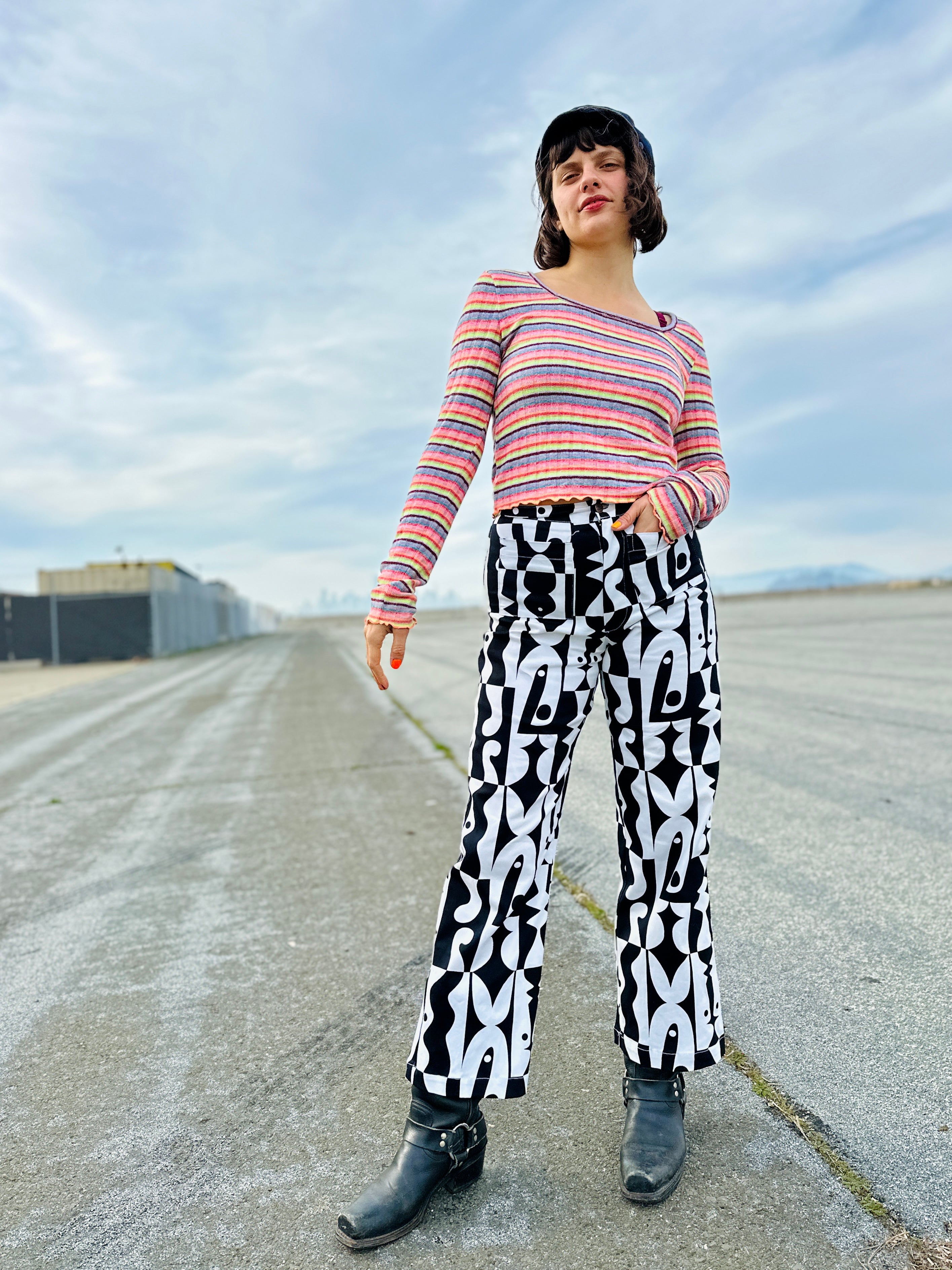 Person wearing a striped shirt and patterned pants standing on an open road with a blue sky.