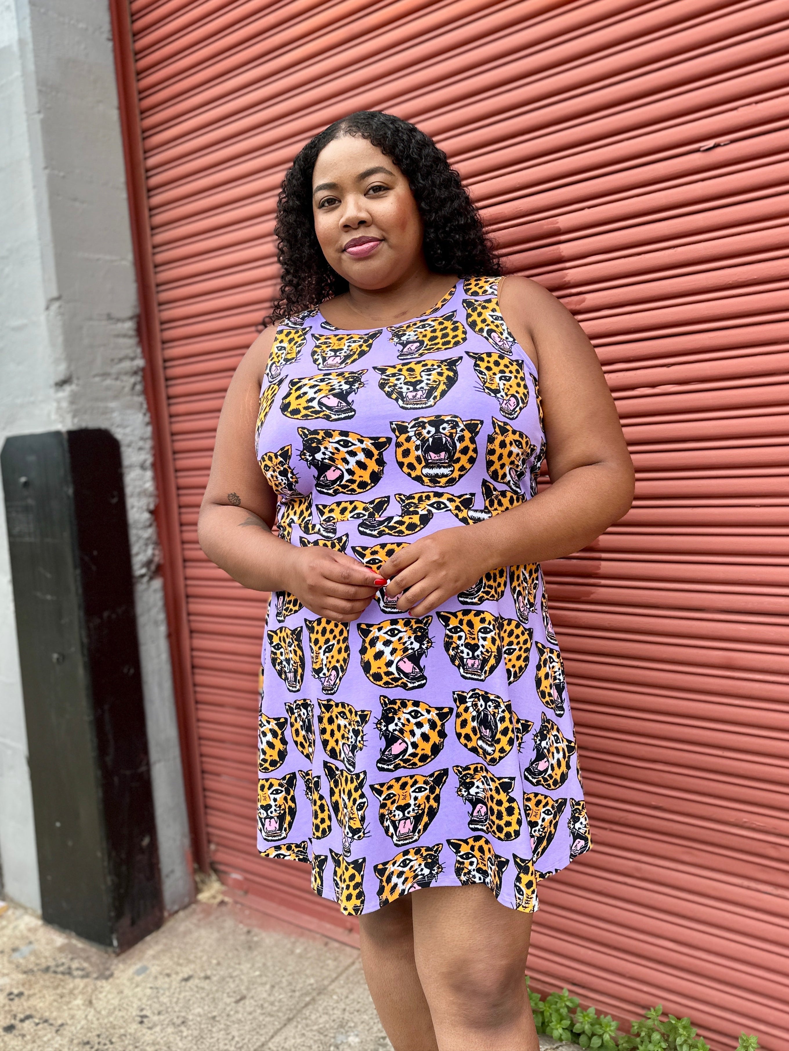 Woman wearing a purple dress with yellow pattern standing in front of a red metal shutter.