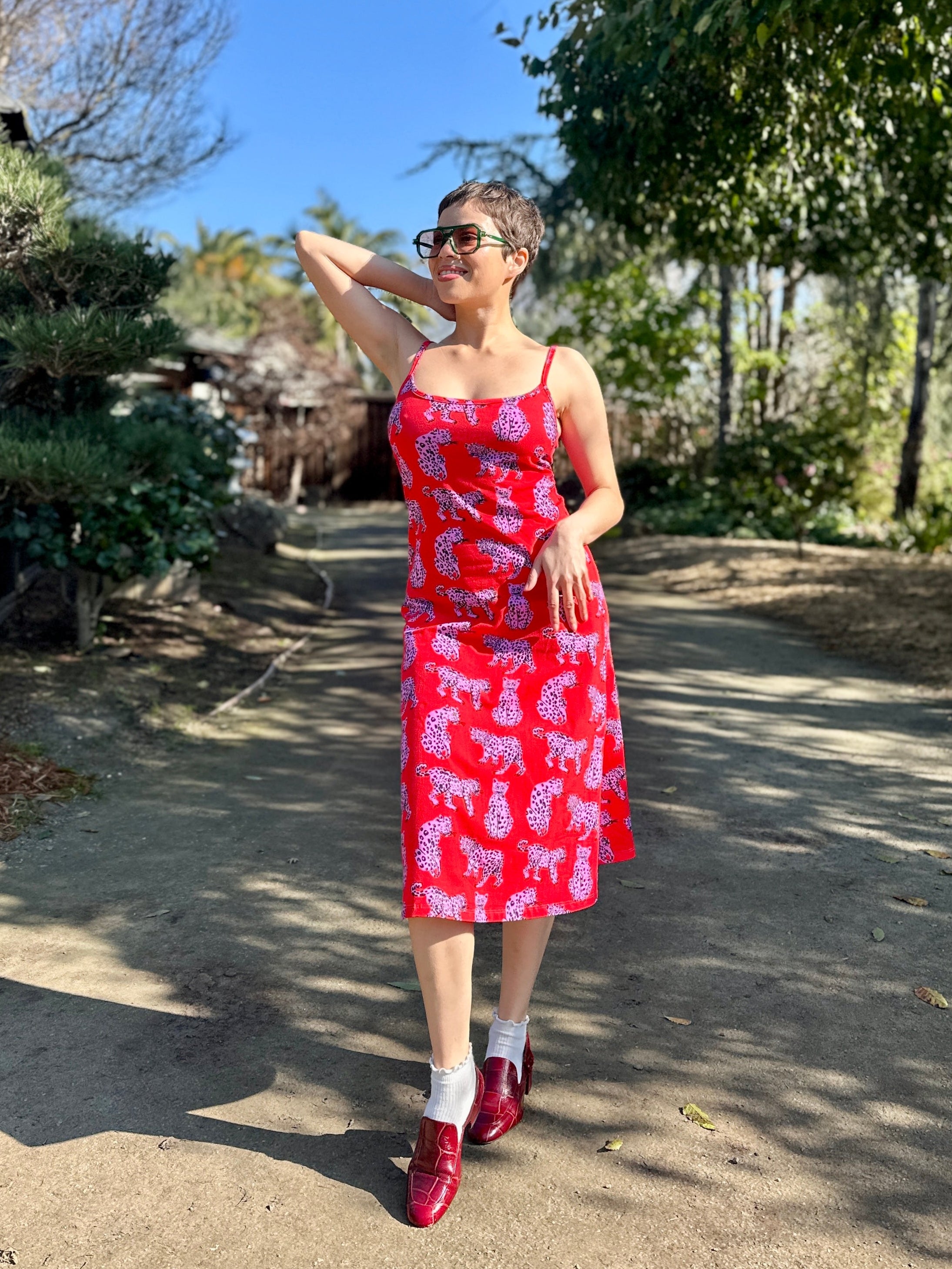 Woman in a red dress with pink patterns standing outdoors on a sunny day.