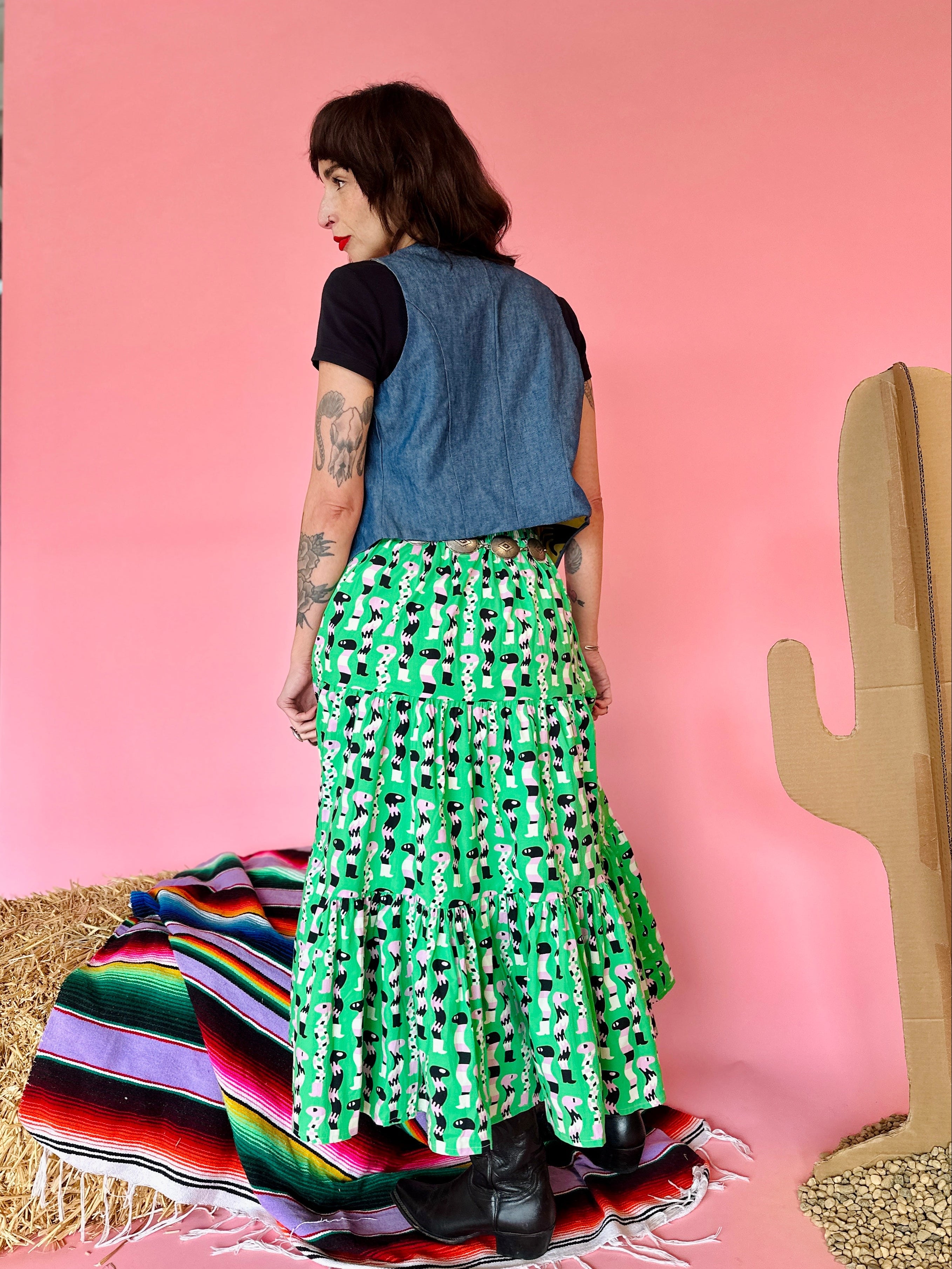 Person wearing a green patterned skirt and denim top against a pink wall.